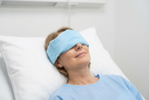 Woman recovering from eyelid surgery with cold compress in Bakersfield clinic
