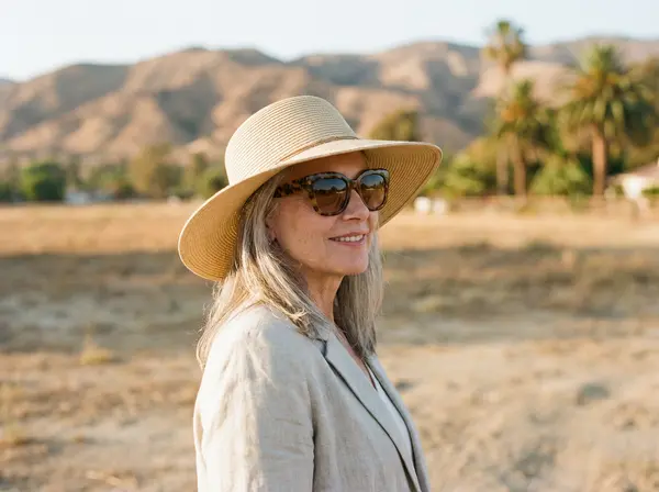 Woman protecting under-eye area from Bakersfield sun exposure with hat and sunglasses after tear trough treatment